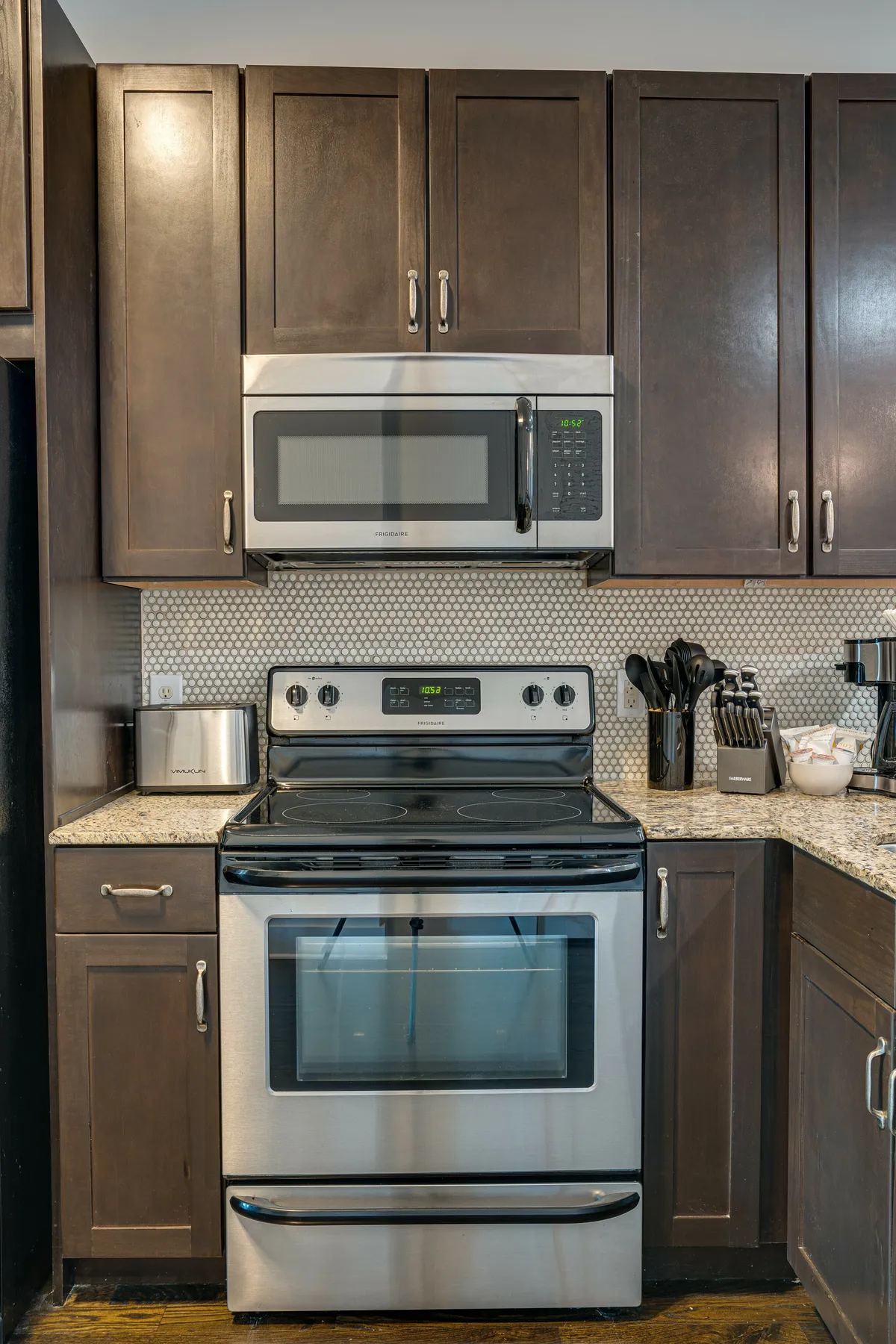 A close view of the kitchen area featuring a stainless steel stove, microwave, granite countertop, and kitchen utensils. The scene is well-lit and efficient, clearly showing the practical amenities for meal preparation and group dining.