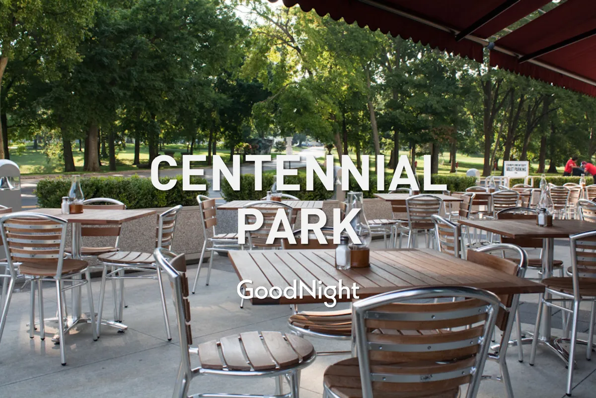 An inviting exterior of Centennial Park, highlighting outdoor dining tables under leafy trees, a winding pathway, and relaxed social gatherings taking place in a lush green setting.