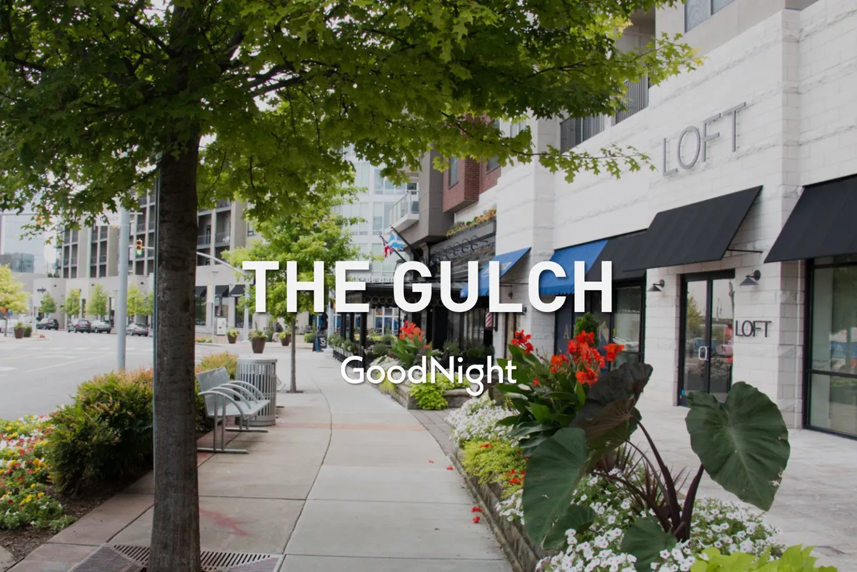 This exterior image showcases lively city streets with benches, planters filled with colorful flowers, storefronts, and trees lining the sidewalk. People walk and gather, creating a vibrant, social atmosphere that mirrors the energetic scene described in the content.