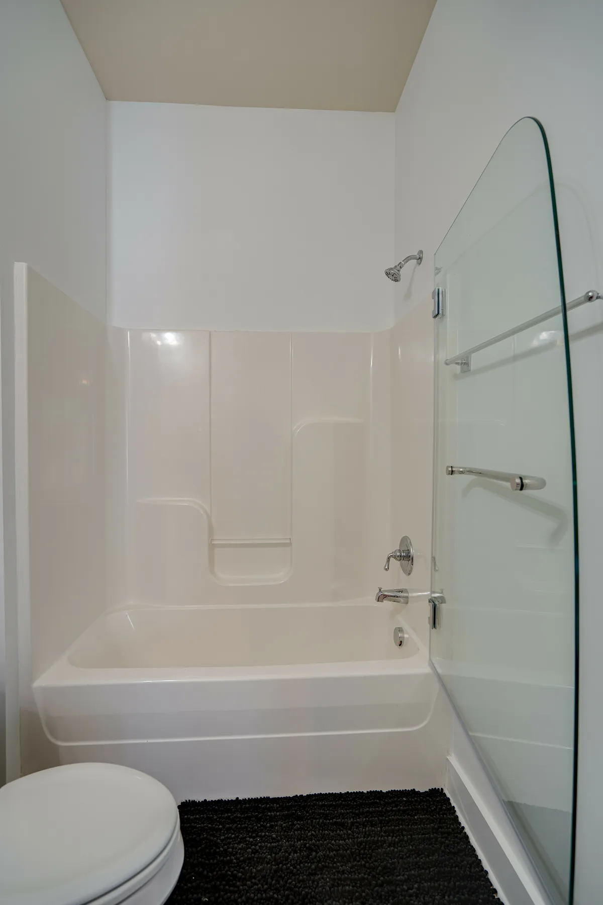 A modern, clean bathroom is shown with a glass-enclosed shower, bathtub, toilet, and floor mat. The space feels fresh and inviting, ideal for relaxation or self-care routines.