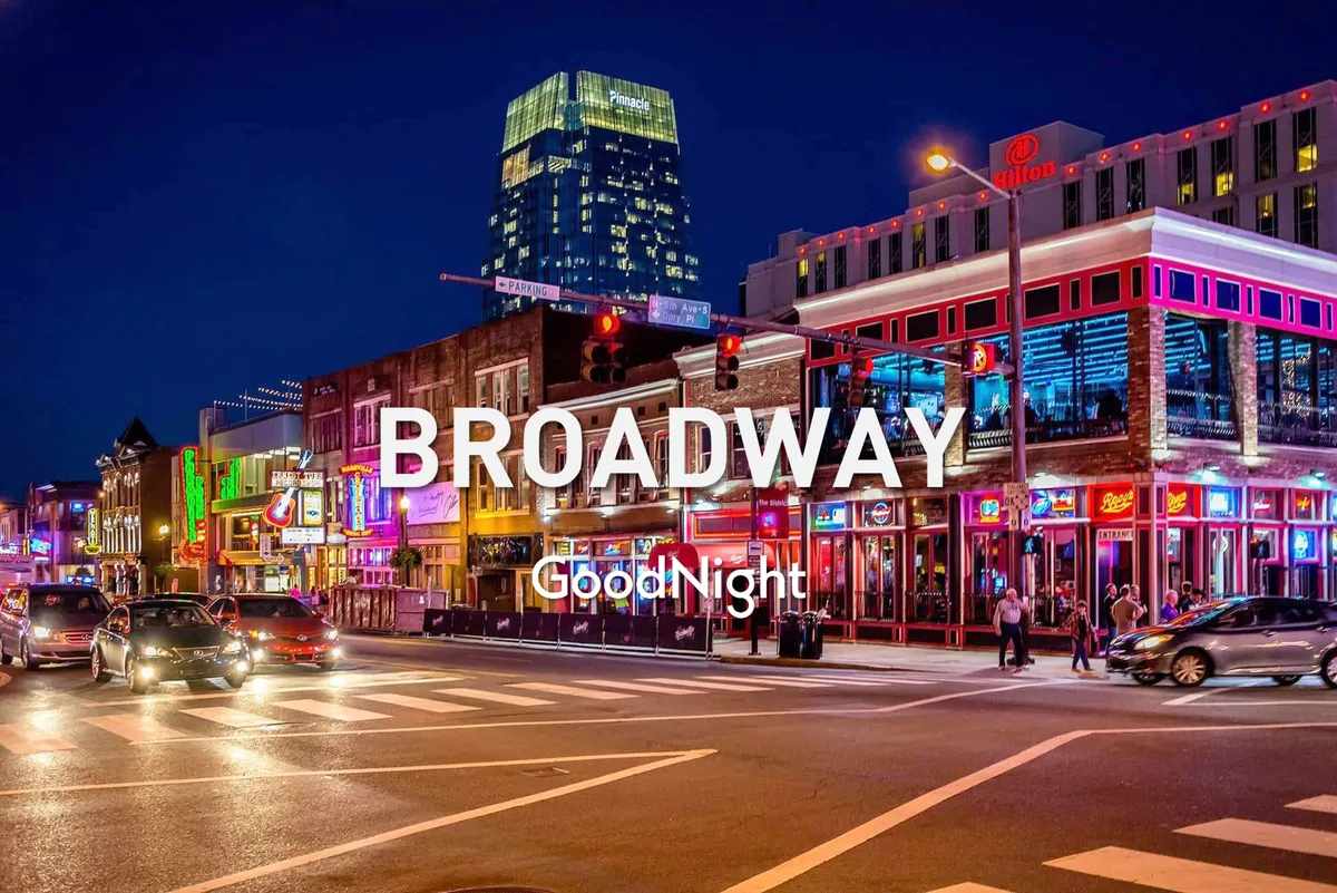 A lively exterior street scene featuring neon signs, busy sidewalks, people strolling, and a high-rise building—all illuminated under the evening sky. The image captures the festive and energetic nightlife that defines Nashville.