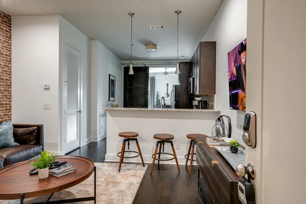 A welcoming living room with a brown leather sofa, wooden coffee table, bar stools, and a kitchen counter in view. The space feels both cozy and contemporary, ideal for movie marathons or game nights as described in the section. The arrangement invites gatherings and shared moments.